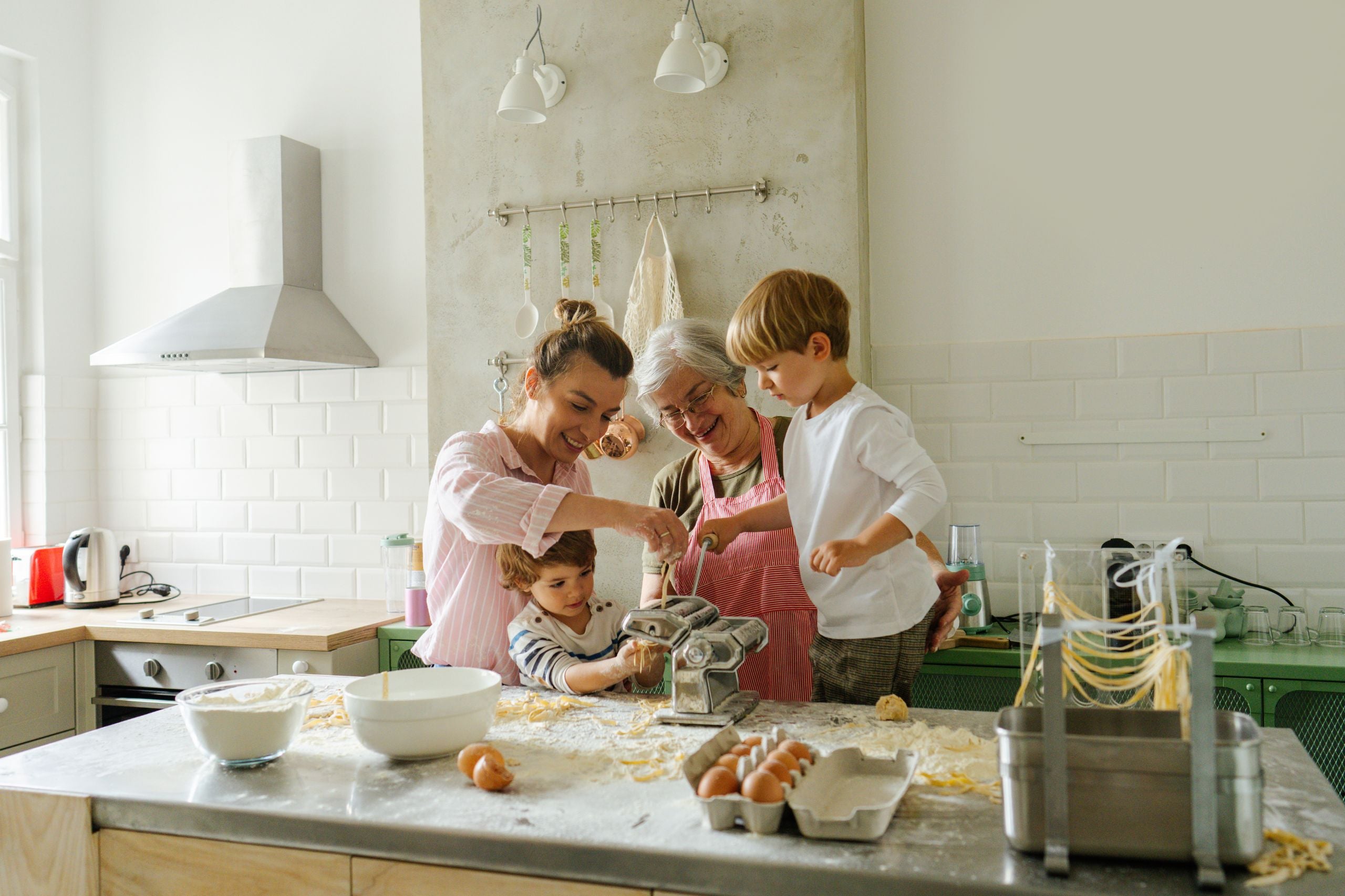 Drei Generationen einer Familie machen gemeinsam Pasta in der Küche, mit einer Nudelmaschine auf der Arbeitsplatte